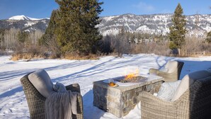 Un área de estar al aire libre cubierta de nieve, con sillas de mimbre y un pozo de fuego de piedra.
