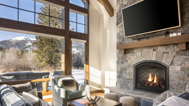 Una sala de estar acogedora con chimenea de piedra, asientos cómodos y un amplio ventanal con vistas a la montaña.