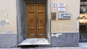 Une porte en bois à deux battants, précédée d’une petite marche, une enseigne au-dessus de la porte et une boîte aux lettres fixée au mur, sur la droite.