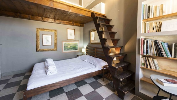 Une chambre avec un sol à carreaux, un lit en bois, un escalier et une bibliothèque.