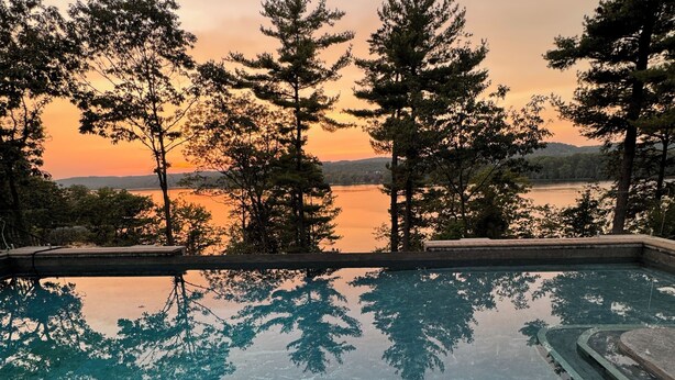 A swimming pool with a view of trees and a sunset.