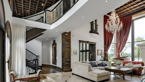 A spacious living area with a high ceiling, a staircase, and a chandelier.