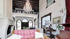 A spacious living room with a fireplace, a chandelier, and a high ceiling.
