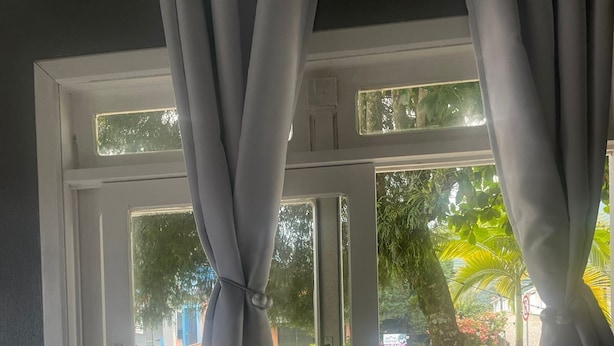 A room with a window, curtains, a small table with a book, a card, and a phone. - Hostel Portal Pomerode (Pomerode)