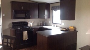 A compact kitchen with dark cabinetry, a stove, a microwave, and a sink. - Charming and Cozy 3-bedroom cottage w/AC, WiFi in enchanting Niagara-on-the-Lake (Niagara-on-the-Lake)
