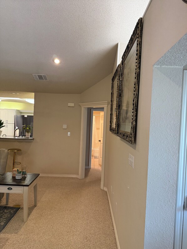 A spacious living area with a kitchen in the background, a dining table, and a hallway leading to another room.
