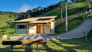 A small house with a tiled roof, a front porch, and a paved driveway leading to a wooden bench. - The Green House of Cunha (Sao Paulo)