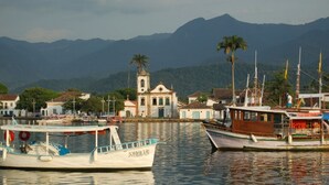 A harbor with boats, a church, and mountains in the background. - The Green House of Cunha (Sao Paulo)