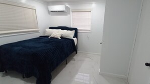 Een slaapkamer met een bed, witte muren, een raam met zonwering en een airconditioning.