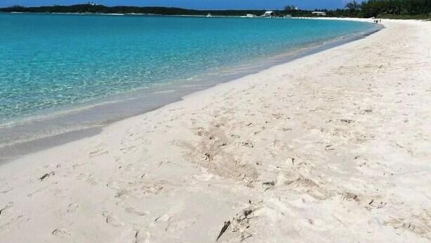 Een strand met helder turquoise water, wit zand en een strakblauwe lucht.