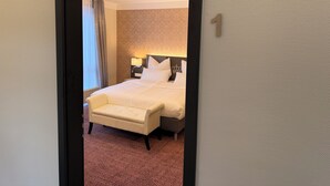 Et hotelværelse med en seng, et natbord, en lampe, en stol og et tæppe med et mønster.