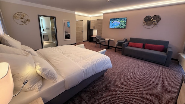 Et hotelværelse med en stor seng, en grå sofa med røde puder, et lille bord og et fjernsyn på væggen.