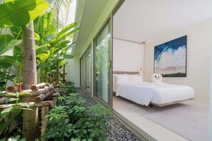 Une chambre d’hôtel moderne avec un grand lit, un tableau au mur et une vue sur un jardin tropical.