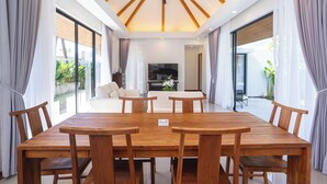 A spacious dining area with a wooden table and chairs, a ceiling fan, and large windows with curtains.