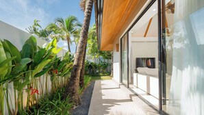 A modern building with a glass facade, a concrete pathway, and tropical vegetation.