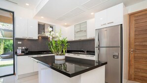 A modern kitchen with white cabinets, a black countertop, a stainless steel refrigerator, and a wooden door.