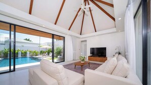 A modern living room with a pool, white sofas, a TV, and a ceiling with wooden beams.