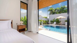 A bedroom with a large bed, a nightstand, and a view of an outdoor swimming pool through large windows.