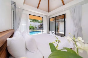 A bedroom with a large bed, a view of a swimming pool, and a sliding glass door leading to a balcony.