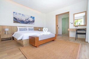 Ett modernt hotellrum med en säng i trä, en stor tavla, en spegel och ett badrum som syns genom en öppen dörr.