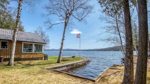 A lakeside cabin with a dock, a picnic table, and a flagpole with an American flag. - 🐾 Mooselodge | Cozy Cabin on Rangeley Lake, Pet Friendly (Rangeley)