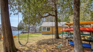 A cabin with a swing set and canoes stored under a tree. - 🐾 Mooselodge | Cozy Cabin on Rangeley Lake, Pet Friendly (Rangeley)