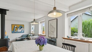 A dining area with a table, chairs, a vase of flowers, pendant lights, a stove, and artwork on the walls. - Cozy fisherman's house near the sea (Rønne)