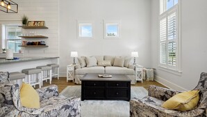A living room with a sofa, two side tables, a coffee table, and a kitchen area with a bar counter and stools.