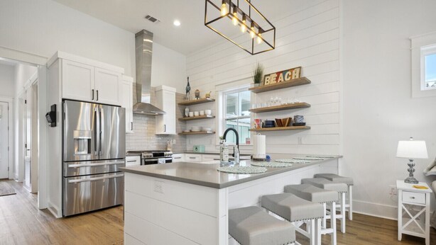 A modern kitchen with white cabinetry, a stainless steel refrigerator, a built-in oven, and a central island with bar stools.