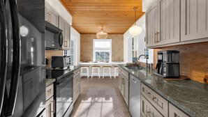 A modern kitchen with a wooden ceiling, stainless steel appliances, and a large window providing natural light. - ⚓Dolphin Cabin! Screened Pool, Dock & More! ⚓ (Bradenton)