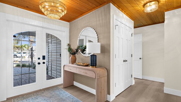 A hallway with a wooden desk, a mirror, and a lamp. There are two white doors and a glass door leading outside. - ⚓Dolphin Cabin! Screened Pool, Dock & More! ⚓ (Bradenton)