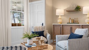 A cozy living room with striped armchairs, a coffee table with decorative items, a bookshelf with books and a plant, and a white door with a window. - ⚓Dolphin Cabin! Screened Pool, Dock & More! ⚓ (Bradenton)