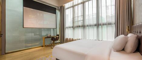 Une chambre d’hôtel moderne avec un grand lit, un bureau avec une chaise et une grande fenêtre avec des rideaux.