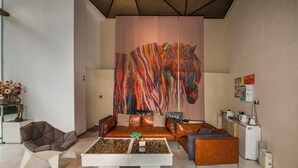 Un salon moderne avec un grand tableau abstrait, un canapé en cuir marron, une table basse blanche et un petit coin cuisine.