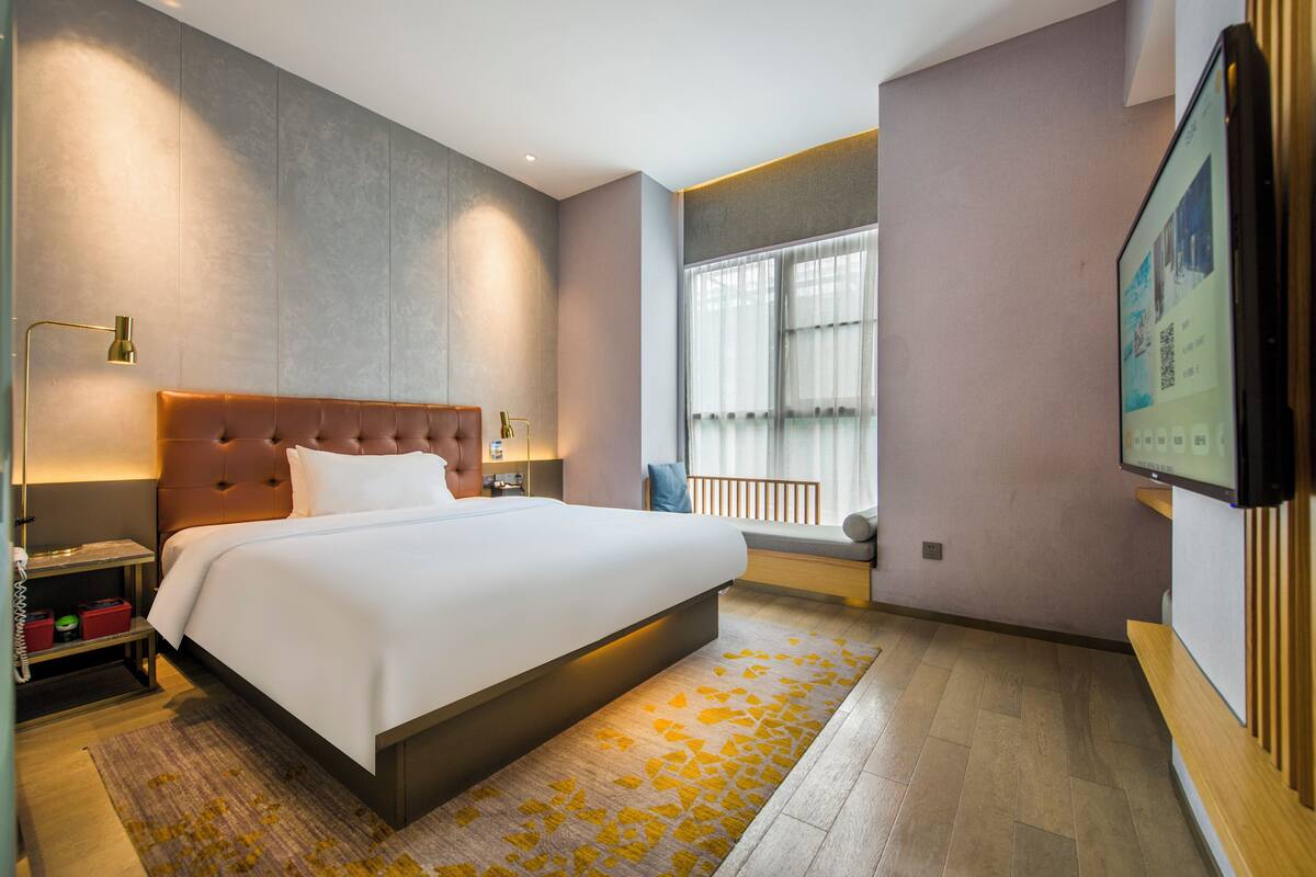 A modern hotel room with a large bed, a television, and a window with a view.