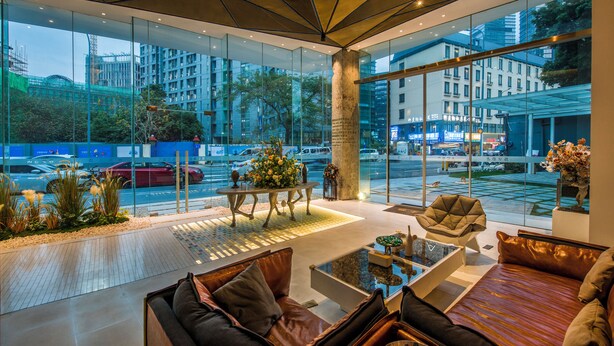 Un intérieur moderne avec un mur de verre donnant sur le paysage urbain, un espace salon central et une table basse.