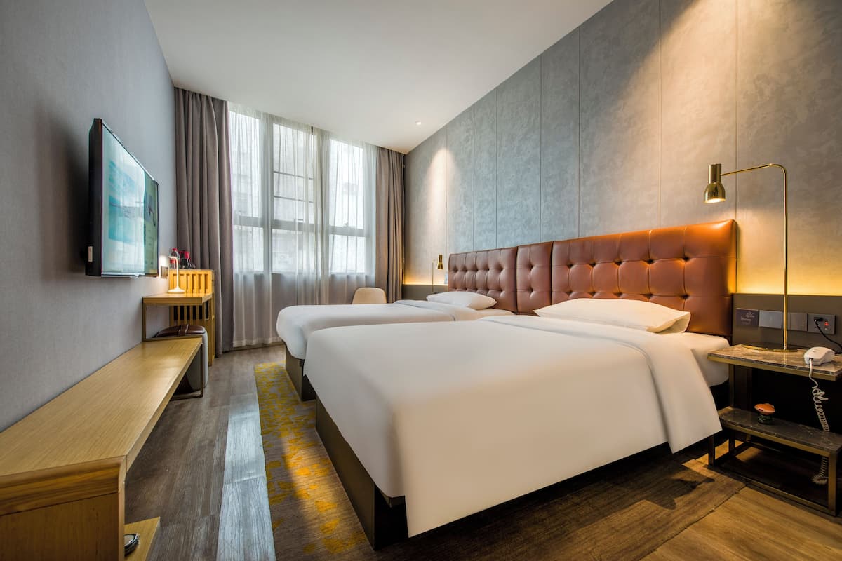 A hotel room with two beds, a TV, a desk, and a lamp.