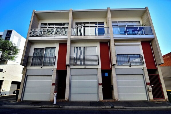 A multi-story building with two garage doors, a balcony on the upper floor, and a red accent wall.