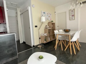 A modern kitchen with a white countertop, a dining area with a white table and chairs, and a small potted plant on a white table.