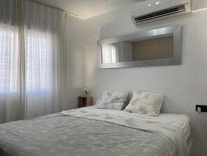 A bedroom with a bed, a bedside table, a mirror, and an air conditioning unit.