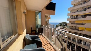 Ein Balkon mit zwei Stühlen, einem Tisch und Blick auf das Meer und die Gebäude.