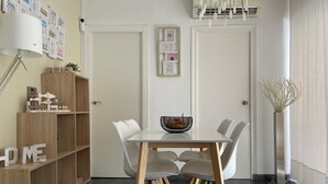 Ein Essbereich mit einem weißen Tisch, Stühlen, einem Holzregal und einer Wand-Klimaanlage.