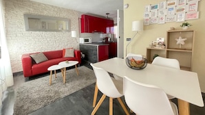 Ein kompakter Wohnraum mit einem roten Sofa, einem weißen Esstisch und einer Küchenzeile mit roten Schränken.