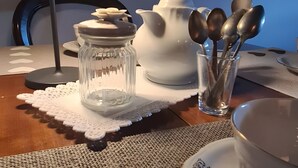 Une table à manger avec un bocal en verre transparent, une théière blanche et un ensemble de cuillères.