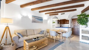 A living room with a sofa, coffee table, and dining area with chairs. There is a kitchen in the background.