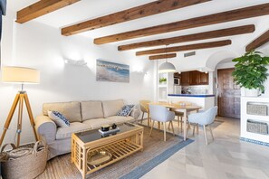 Sala de estar con sofá, mesa de centro y comedor con sillas. Se observa una cocina al fondo.