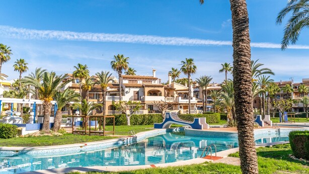 A resort with a swimming pool, palm trees, and Mediterranean-style buildings.