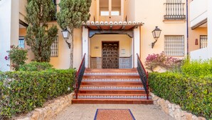 A building with a tiled entrance, a set of stairs leading to a door, and a stone wall surrounding the area.