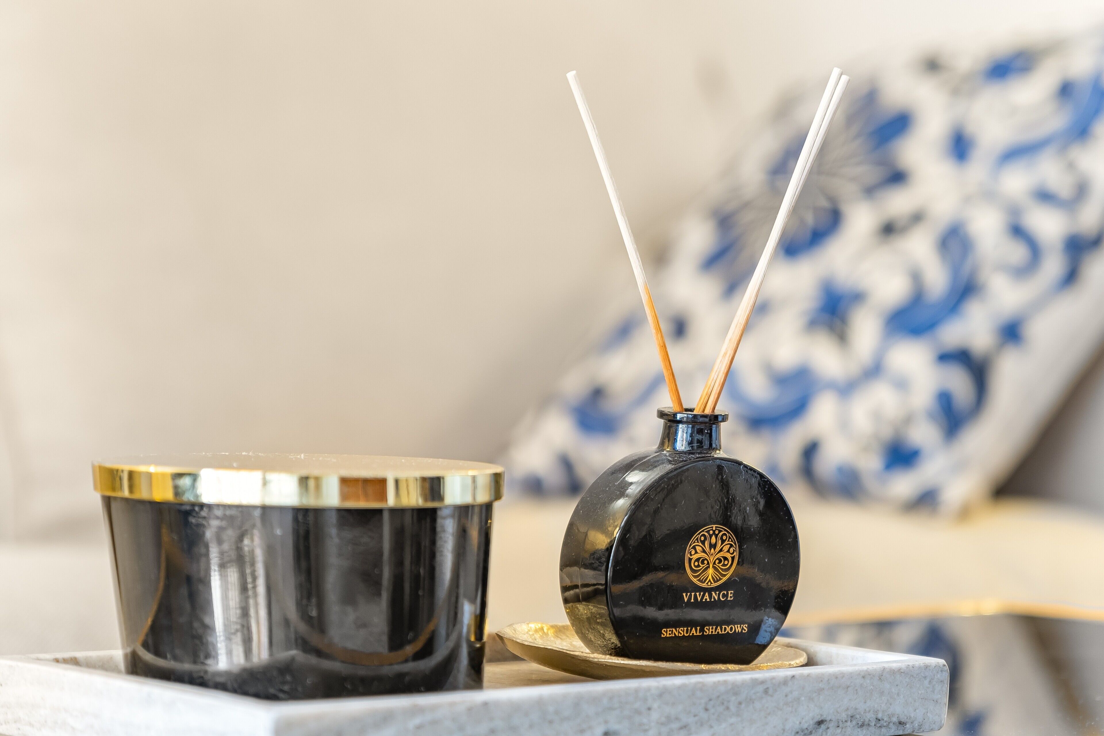 Una vela negra con un emblema dorado y un recipiente metálico con tapa dorada.