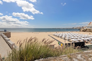 A beach with umbrellas and lounge chairs, a clear sky, and a distant pier. - Cascais City & Sea Apartment with Balcony, Wi-Fi and Air Conditioning (Cascais)